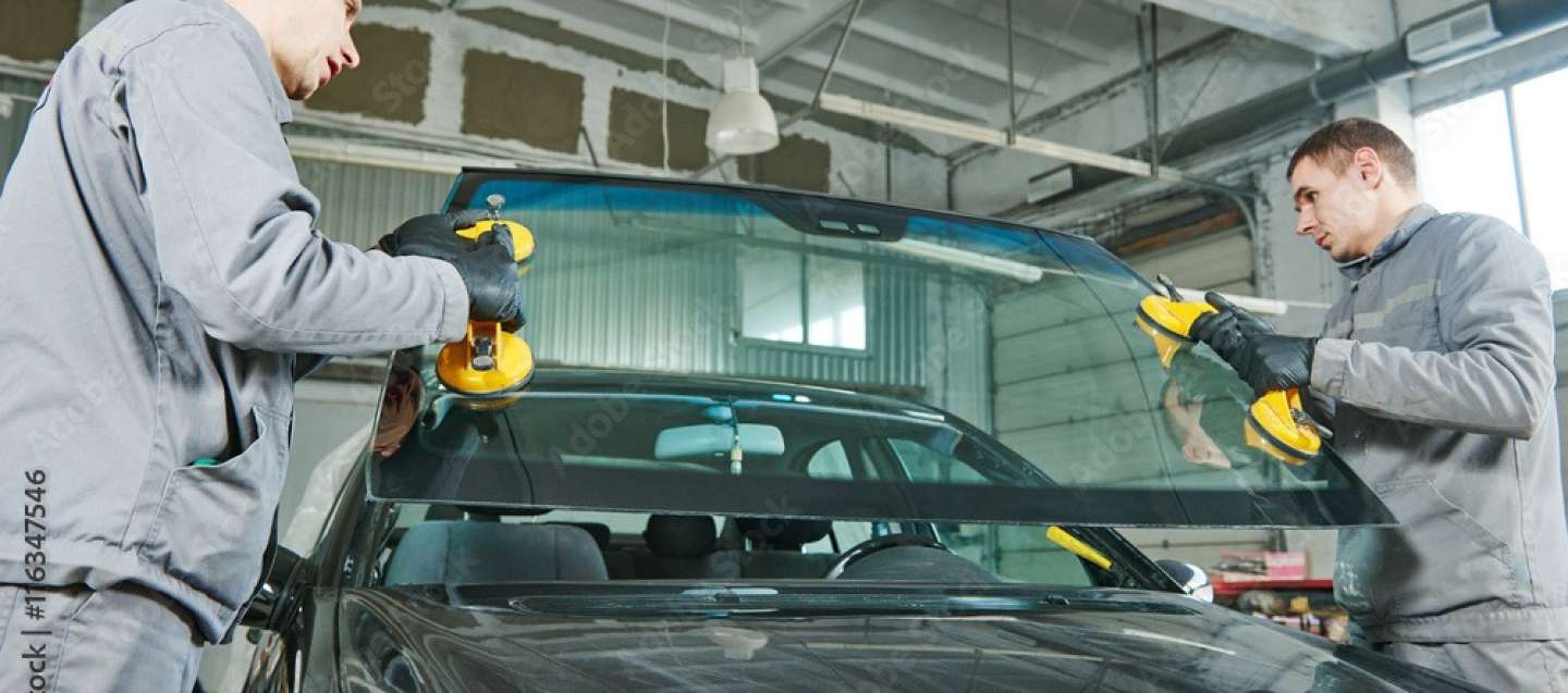 Two auto glass installers setting a new windshield into a vehicle with the old window removed