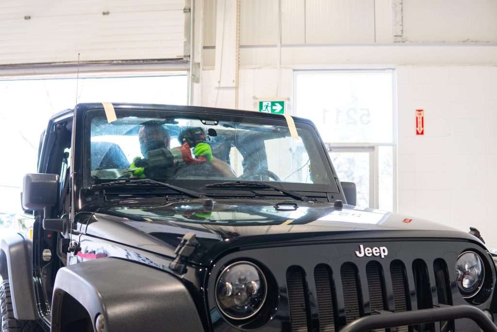 A Windshield Surgeons technician using a power tool in the process of replacing a Jeep Wrangler windshield