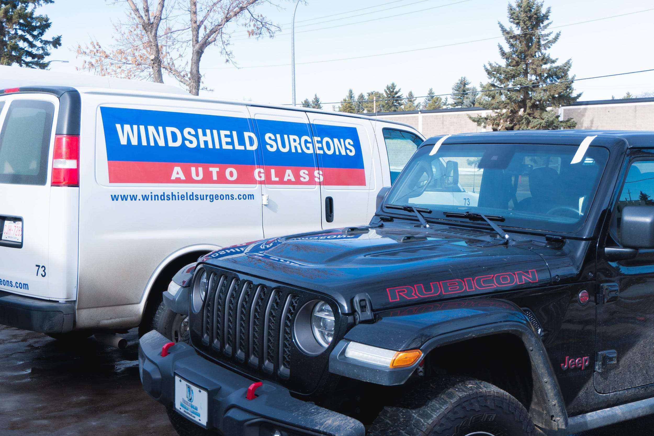 A Jeep Wrangler with a newly-installed windshield parked next to a Windshield Surgeons service van.