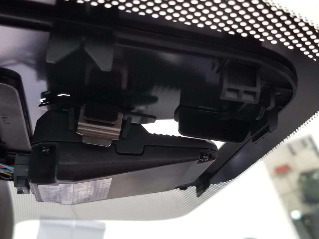 Close-up on the sensor and camera hardware attached to a windshield, used for traffic sign recognition and other ADAS features