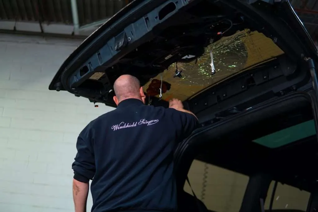Technician wearing a Windshield Surgeons uniform working on the inside of a vehicle’s rear hatch with a shattered back window.