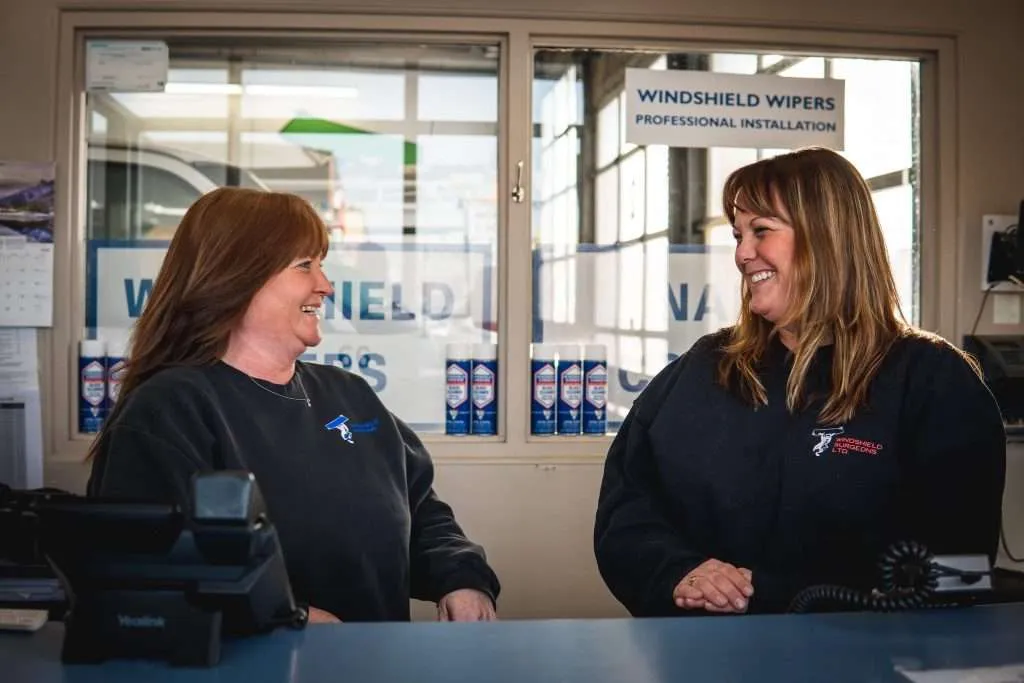 Two female Windshield Surgeons team members smiling at each other, enjoying a warm and positive work environment