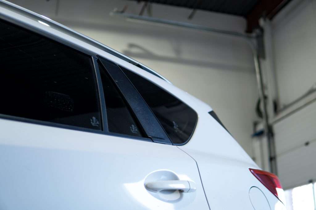 Close-up view of the rear side windows and door of a white SUV, showing black trim and a rear taillight, photographed indoors