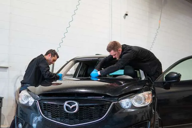 Two Windshield Surgeons technicians working on the windshield of a black Mazda SUV inside an auto glass shop