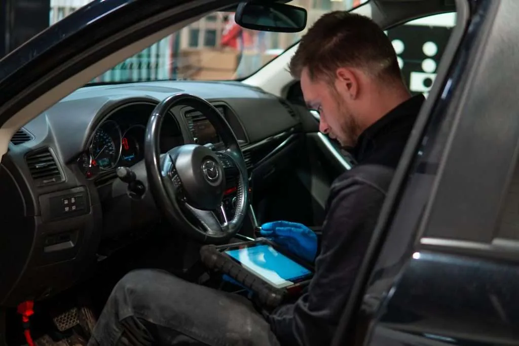Windshield Surgeons technician sitting in the driver's seat of a vehicle, performing ADAS calibration using an iPad