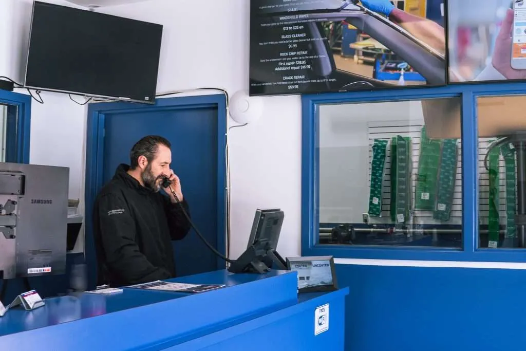 Windshield Surgeons employee speaking on the phone and preparing a quote request at the front desk inside a service center.
