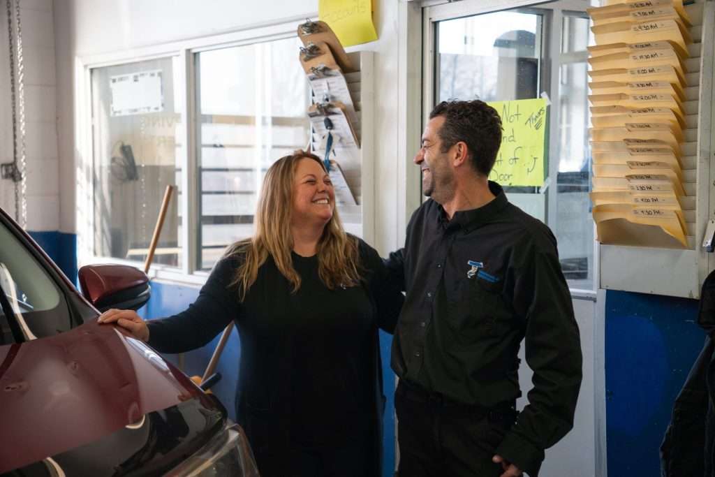 Windshield Surgeons co-workers arm in arm smiling at one another. Looking pleased with their career and team