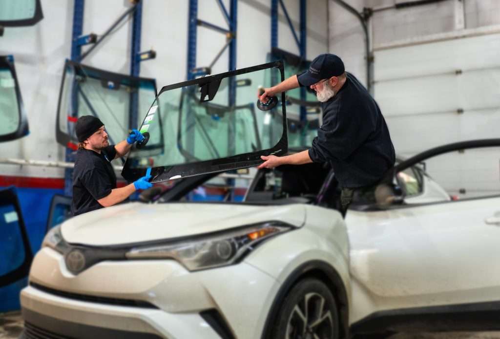 Two Windshield Surgeons technicians maneuvering a windshield replacement into place