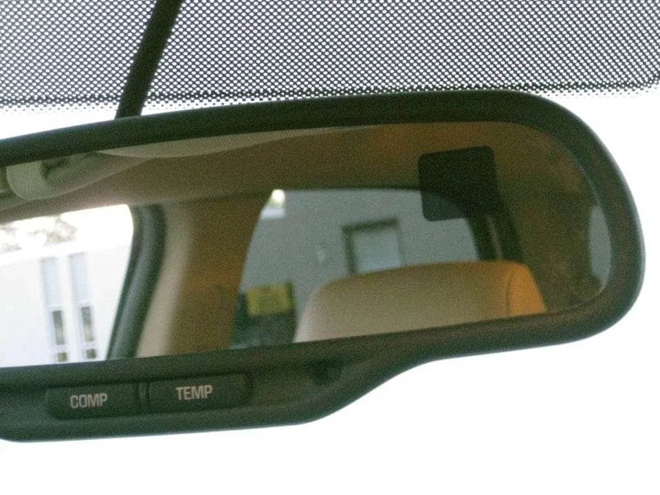 Close-up of an auto-dimming rearview mirror inside a vehicle, showing compass and temperature display buttons.