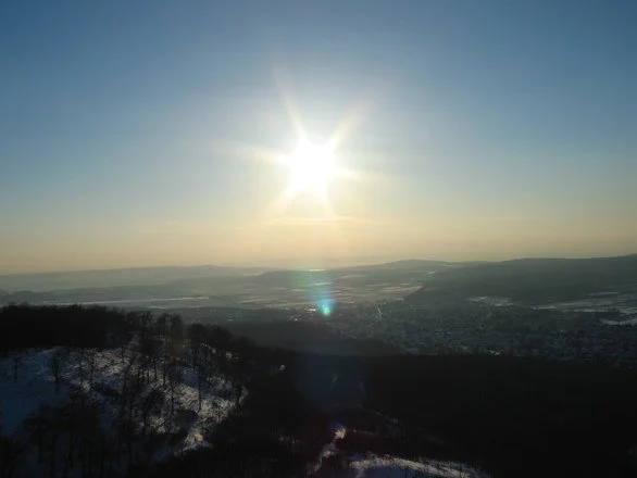 Bright solar glare over a snowy landscape with hills and a distant town.